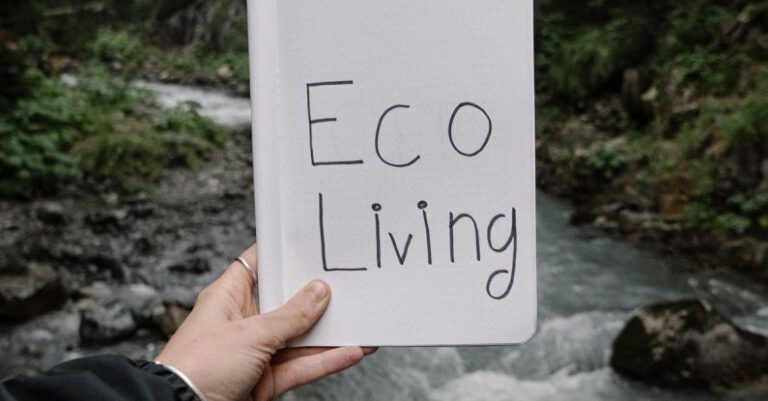Sustainable Living - Person Holding a Notebook with a Text "Eco Living" on the Background of a River in a Forest